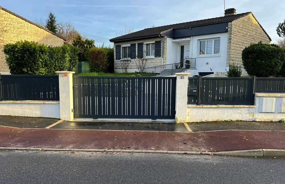 Propriété résidentielle avec portail coulissant en aluminium anthracite à lames verticales, installé entre piliers en béton
