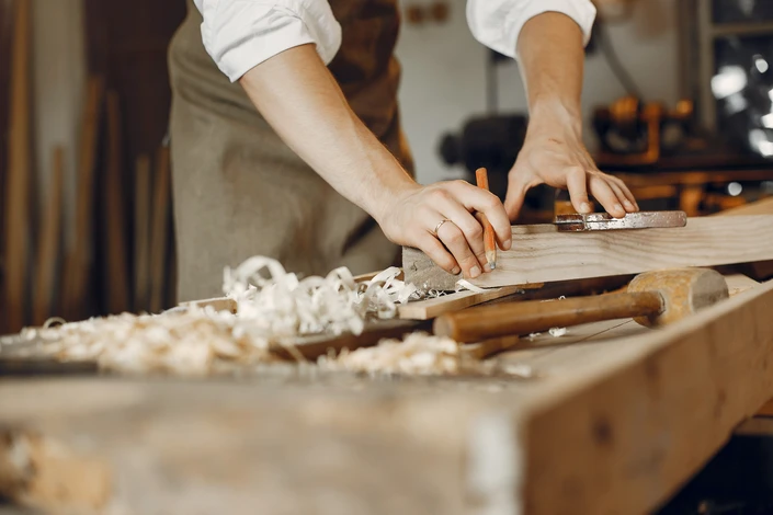 Un artisan en chemise à carreaux utilise un rabot à main sur une pièce de bois dans un atelier de menuiserie
