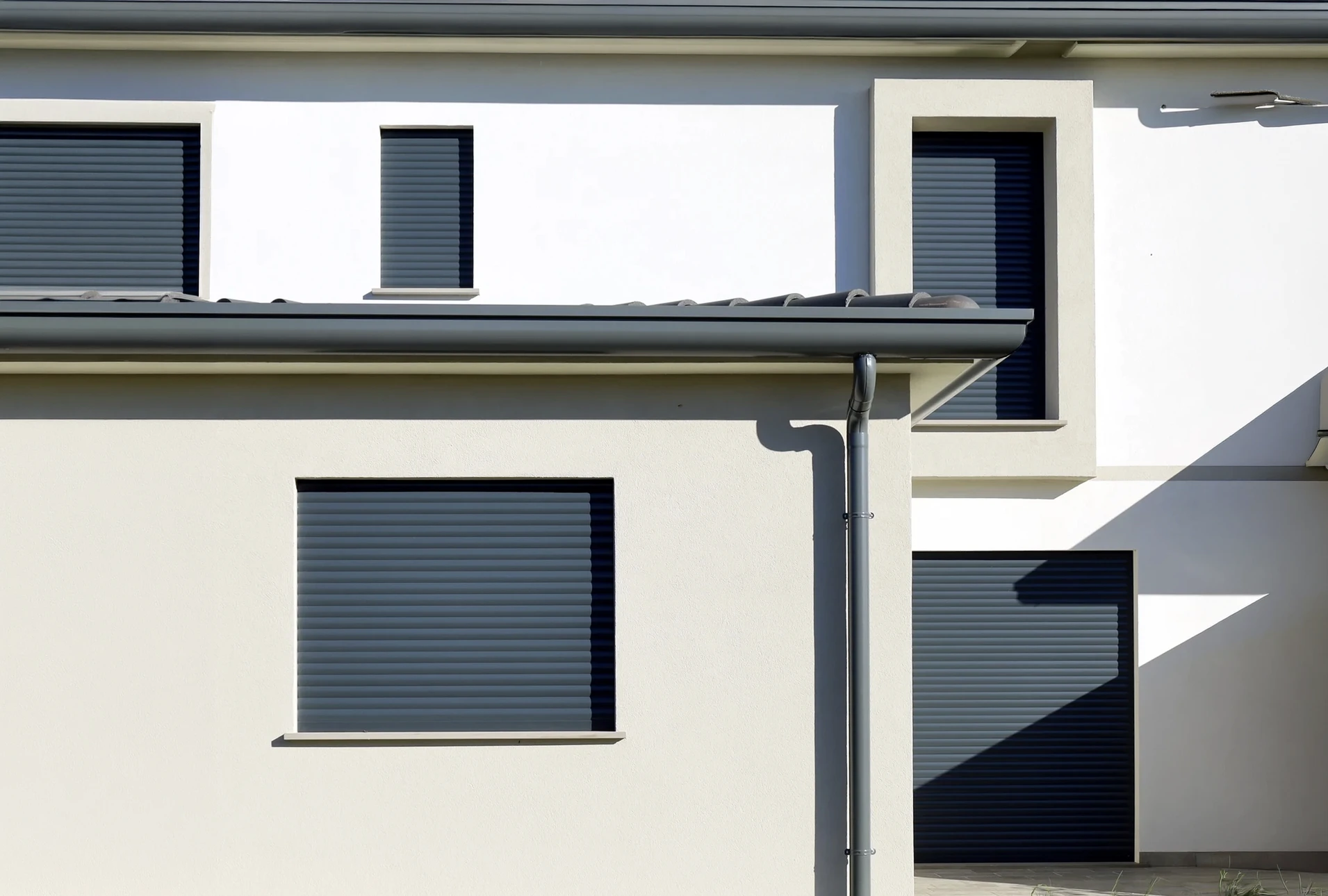 Façade de bâtiment moderne avec volet roulant électrique blanc partiellement fermé sur fenêtre à double vitrage