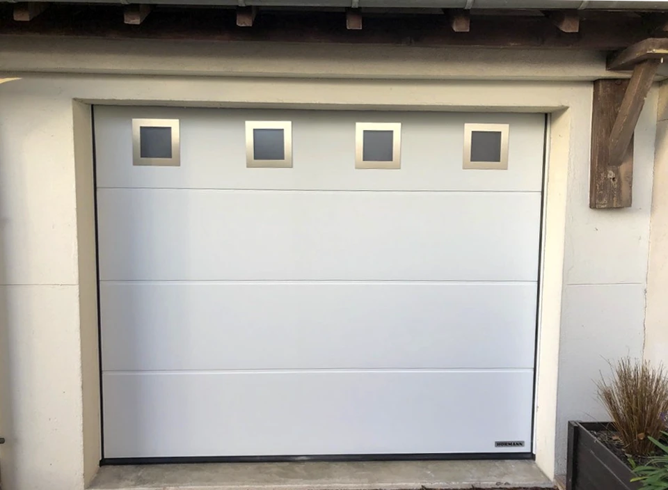 Garage résidentiel extérieur avec deux portes sectionnelles couleur terre cuite, murs blancs et soubassement décoratif en carrelage beige