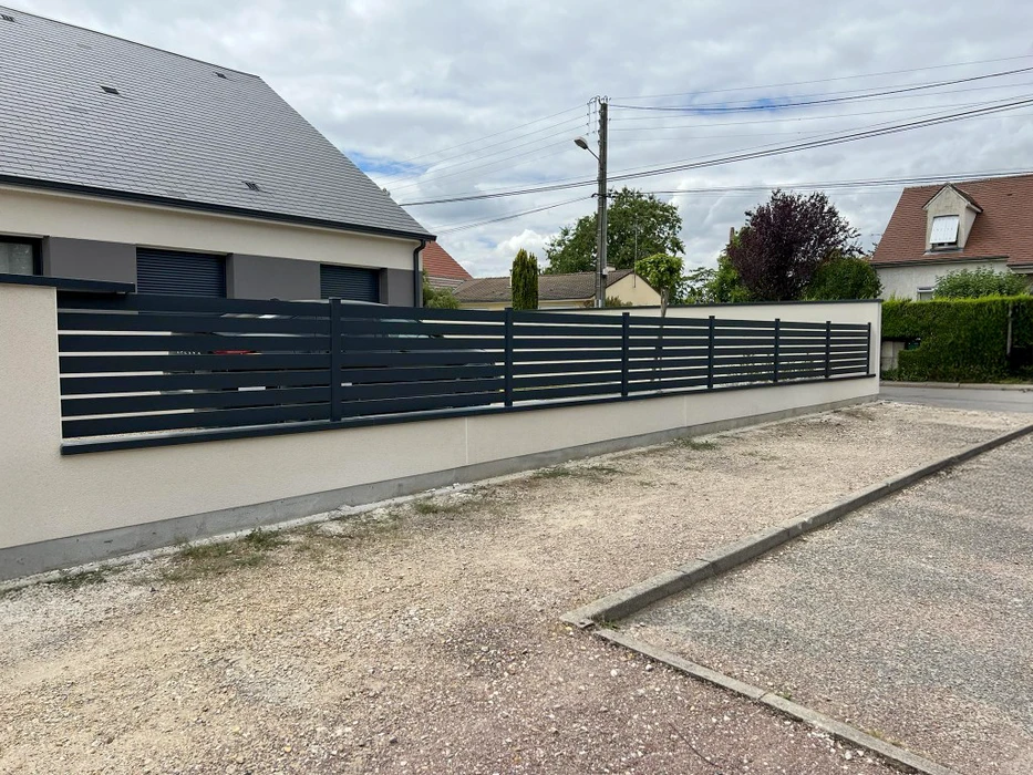 Portail coulissant moderne en aluminium anthracite avec panneaux ajourés et grillage métallique central, installé entre piliers maçonnés blancs sur entrée gravillonnée d'une propriété résidentielle